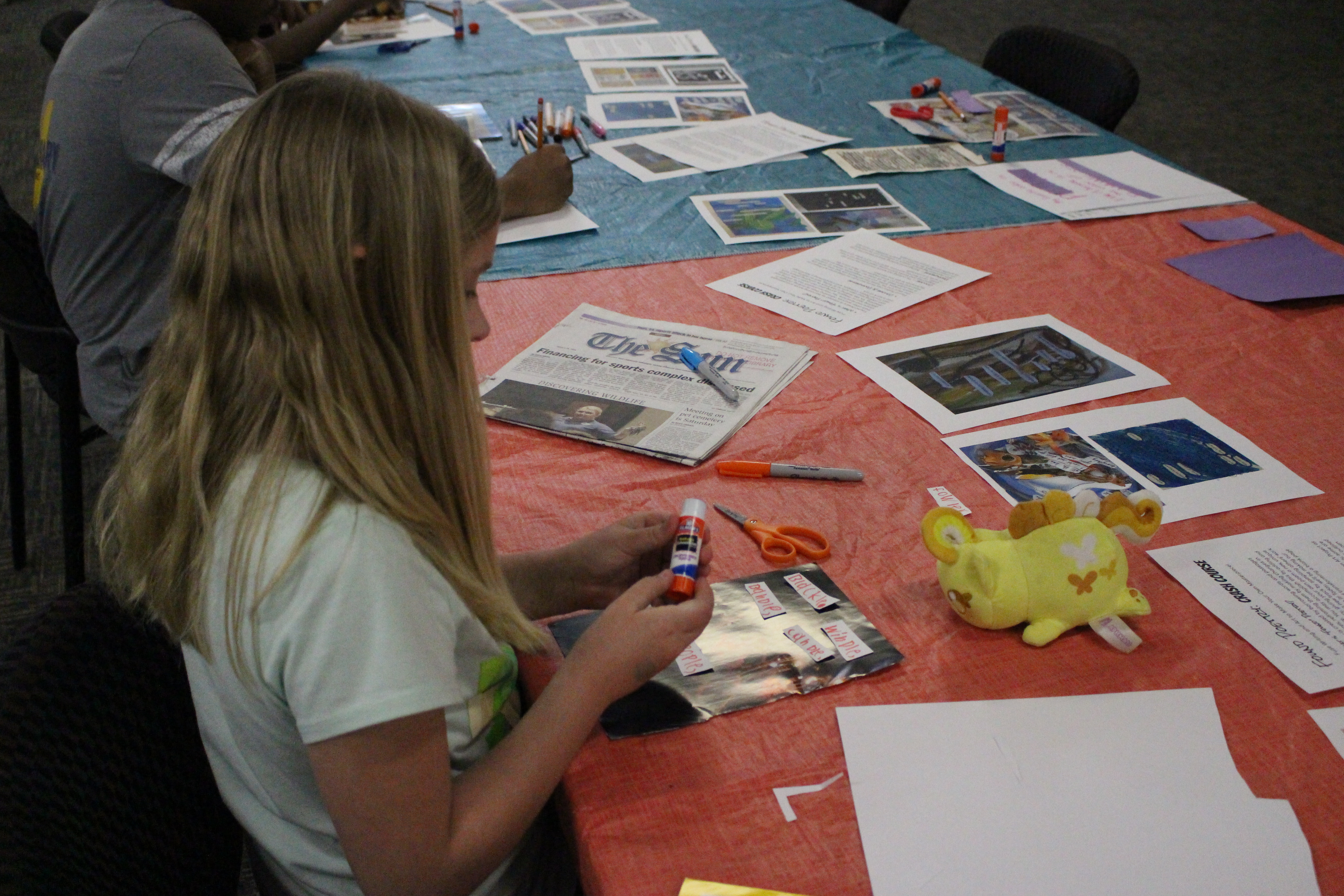 A Tween at a CCJPL tween event uses supplies such as glue, scissors, and newspaper to create a craft. 